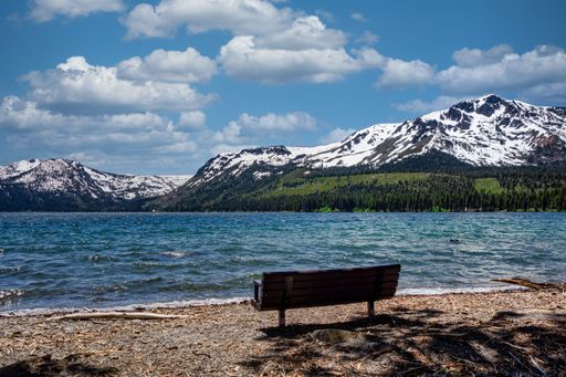 A dramatic shot of an empty wooden bench by Lake Tahoe with mountains the background in the USA