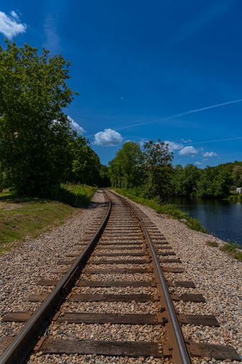 A vertical shot of a railroad passing through trees and lake on a sunny day