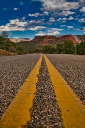 A vertical shot of a gravel road with yellow lines leading to the Red Rocks in Sedona, Arizona