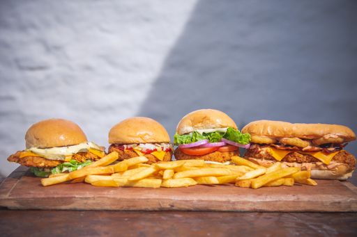 A closeup shot of four burgers with some fries on the side
