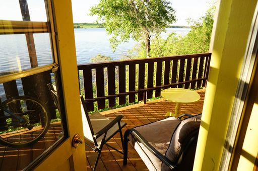 A high angle shot of the balcony with chairs and yellow table on it with a view of a river
