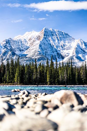 A vertical shot of a mountain in the Canadian Rockies with trees and a lake below