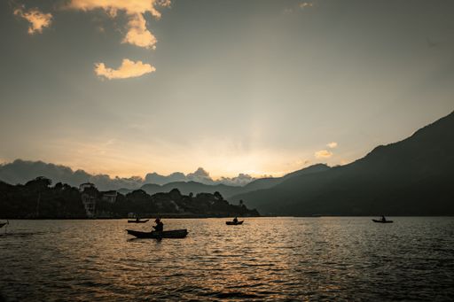 A silhouette shot of people on boats floating on lake Atitlan at sunset with hills in the background