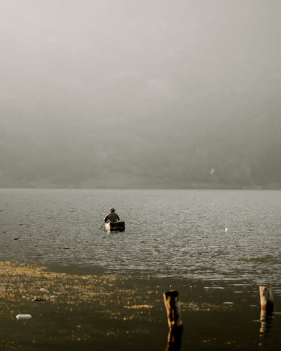 A man in a small boat swimming towards the other coast of lake Atitlan covered in fog