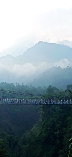 A vertical shot of a suspension bridge over a mountain gorge, in cloudy weather