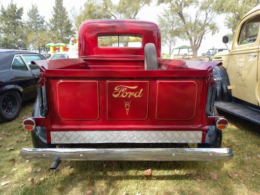 Old red and black utility pickup truck Ford 85 V8 1938 - 1939 in the countryside. Rear view. Brand. Logo. Nature grass and trees. Classic car show.
