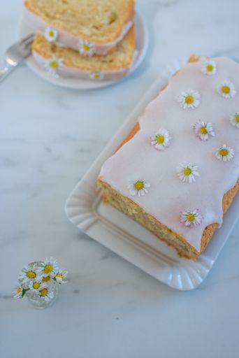 A vertical closeup shot of a vanilla bundt cake with daisies