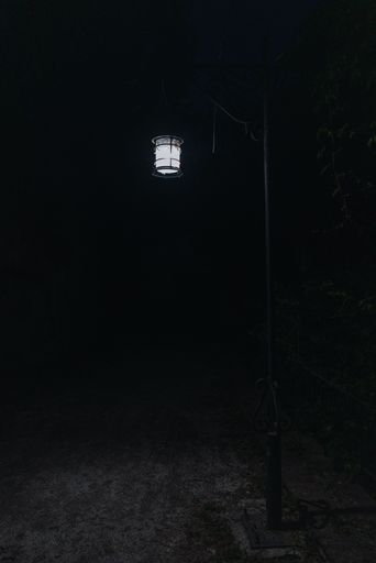 A vertical shot of a small illuminated lamp hanging in a dark area
