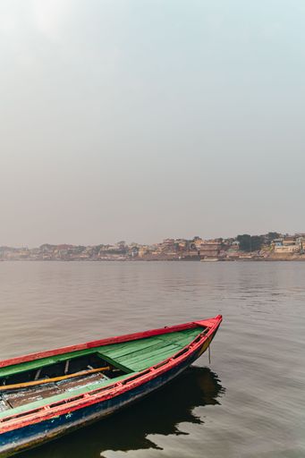 A vertical shot of a part of a colorful kayak in the lake in the background of the cityscape.