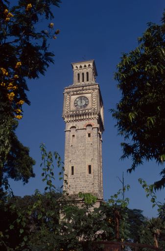 A vertical shot of the Secunderabad Clock Tower surrounded by trees under a clear blue sky