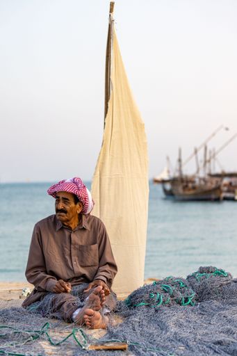 A vertical shot of a local Arabian fisherman sitting on the ground and preparing his fishing net. Doha, Qatar