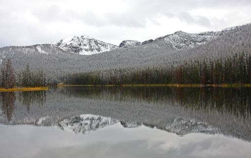 A natural view of a calm lake with trees and mountain landscape reflecting on the water surface