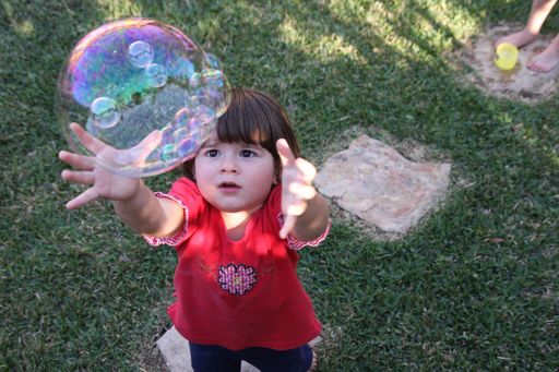 A closeup of a little girl trying to catch the bubble in a park
