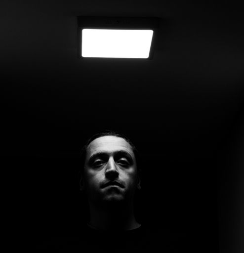 A black-and-white shot of a man standing under the square light in dark room