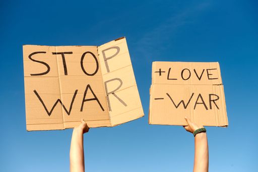A cardboard sign saying more love, less war, and stop war held by two hands