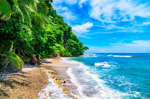 A tropical island on the shore of the ocean with water splashing under the blue sky