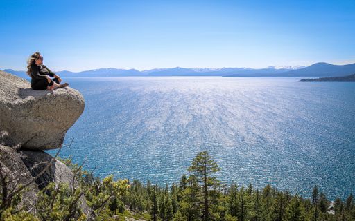 A woman sits atop a boulder taking in the views across Lake Tahoe and the northern Sierra Nevada.