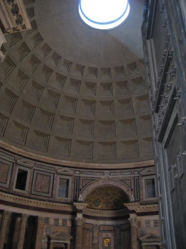 A vertical inside view of a pantheon in Rome with light coming from the dome