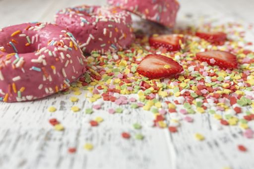 A closeup shot of pink sprinkled donuts and strawberries on white surface