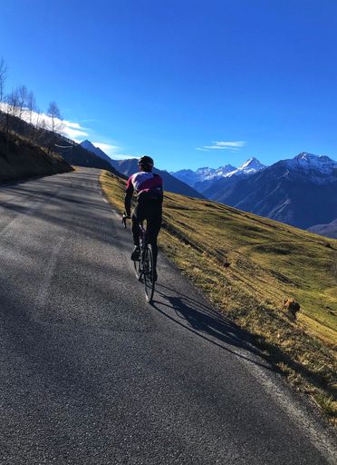 A vertical shot of a male riding a bicycle on a long road in a mountain field - concept for sports and fitness