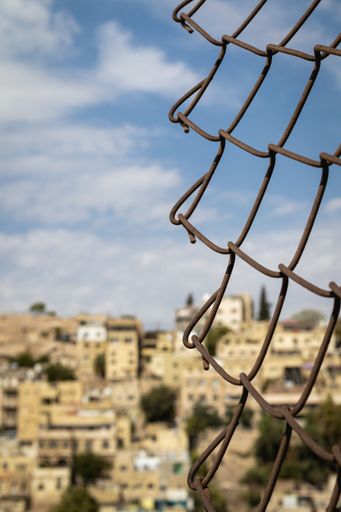 A vertical shot of a Chain link fence in front of a city in Jordan blurred in background