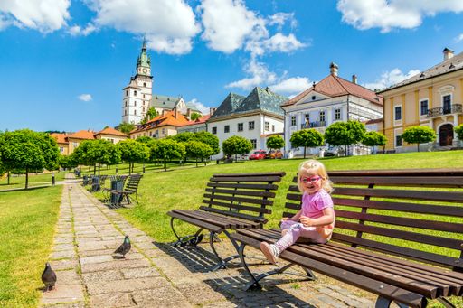A cute Caucasian girl sitting on a bench in golden town Kremnica