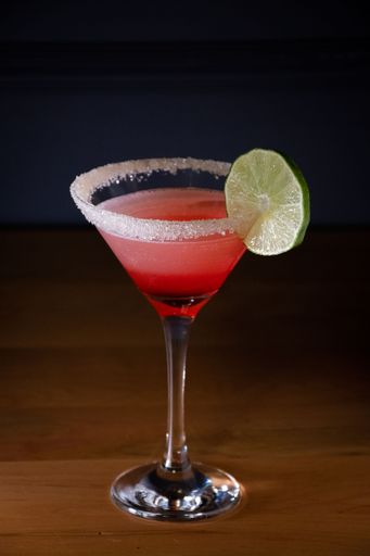 A vertical shot of a glass of cocktail with a lime slice on a wooden table