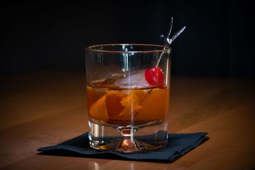 A glass of Old fashioned cocktail on a tablecloth on a wooden table