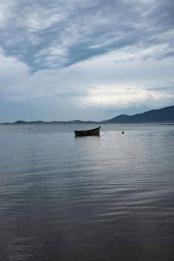 A vertical shot of wooden fishing boat in the lake under a cloudy sky