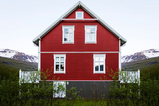 The beautiful facade of a wooden red house with white windows and balconies on a green field