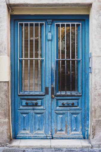 A vertical shot of a wooden blue door on the cement wall of an old building
