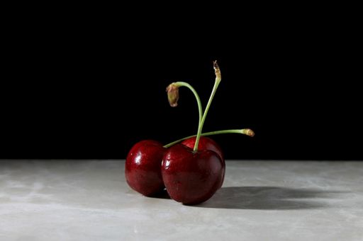 A closeup of red cherries on a white marble table and black background.