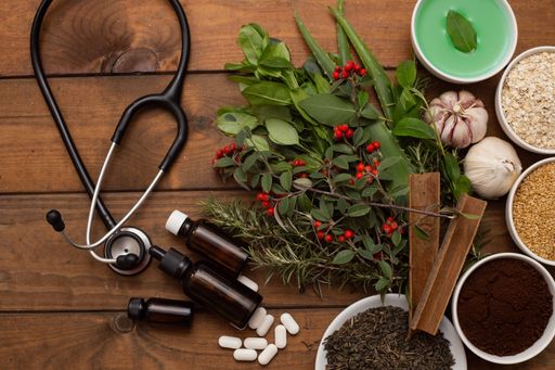A top view of a phonendoscope next to herbs, spices, pills on a wooden surface