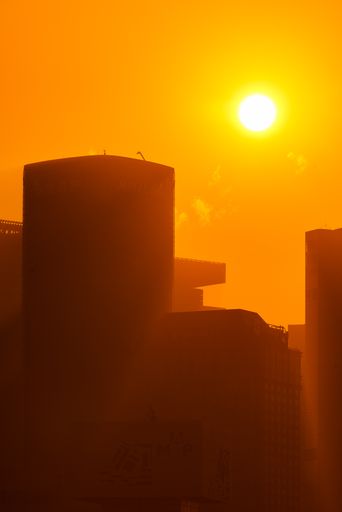 A vertical shot of the silhouettes of buildings in yellow lights during sunrise in Shanghai, China