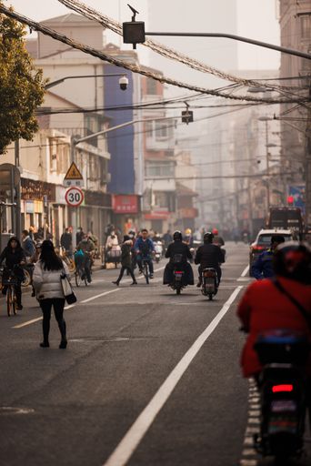 A vertical shot of a road full of people walking and riding scooters or bicycles in Shanghai, China