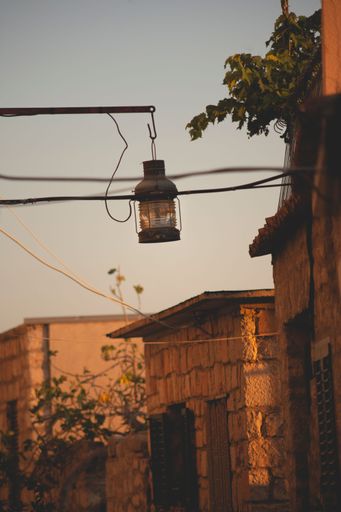 A vertical shot of the street lamp hanging from the pole against the old buildings and sky at sunset.