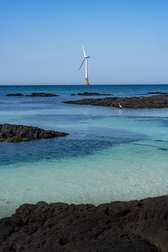 A vertical shot of a windmill along the tropical coast of Jeju Island, South Korea.