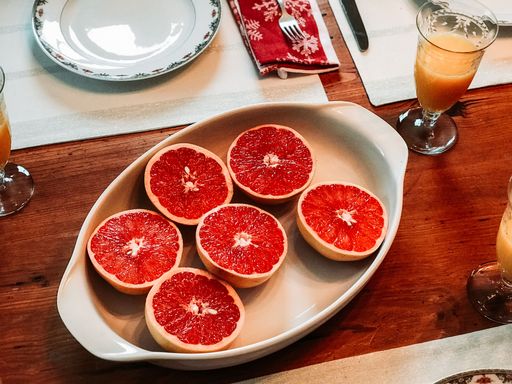 A high angle shot of halved red grapefruits on a table with a glass of orange drink