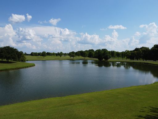 A pond on a clear green field under a bright blue sky with clouds in Montgomery, USA