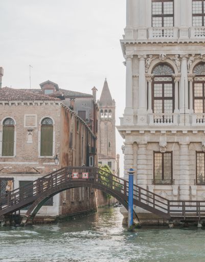 A vertical shot of a canal with a metal bridge against historic buildings in Venice, Italy