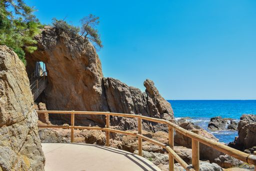 A staircase in a cliff surrounded by handrails and the sea under a blue sky and sunlight