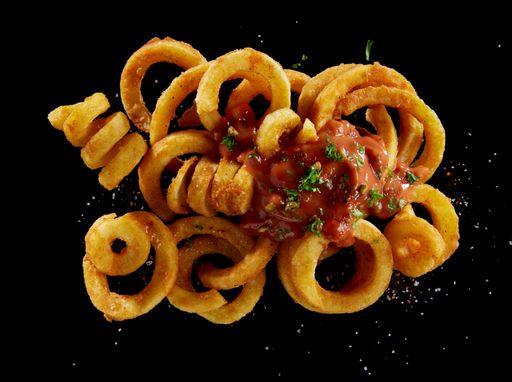 A Top view of appetizing French fries topped with sauce and greens with sprinkled salt isolated on black background