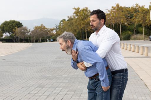 A shot of a young male trying to perform choking first aid to a middle-aged male - giving abdominal thrusts