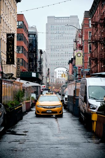 A yellow taxi in the traffic in the street in Little Italy, New York City on a rainy day