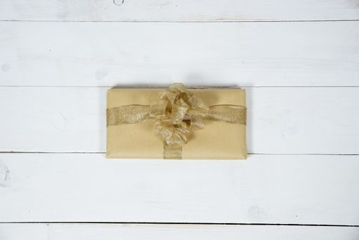 An overhead shot of a present with golden ribbon on a white wooden surface