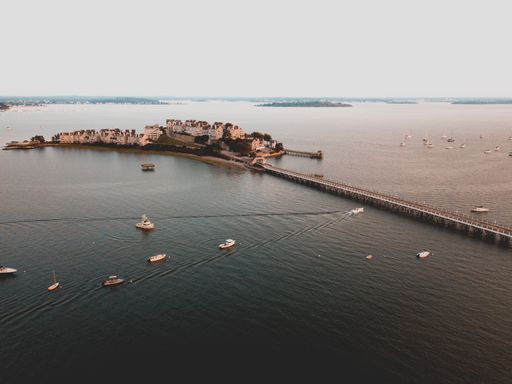 Aerial shot of a bridge and a little populated island in the sea with boats floating around