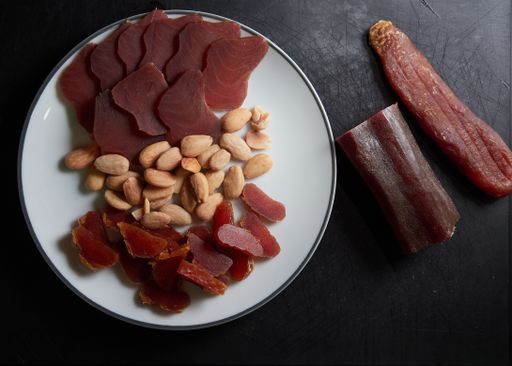 A top view of a plate with dried tuna and dried fish roe with fried almonds on black background