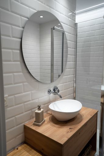A vertical shot of circle mirror on white wall with sink and water tap below in bathroom
