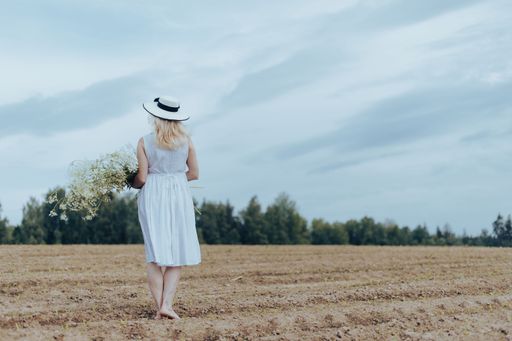 A beautiful blonde woman wearing a hat and a white dress holding flowers in a field