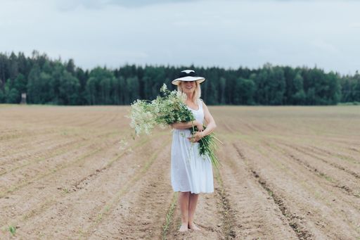 A beautiful blonde woman wearing a hat and a white dress holding flowers in a field